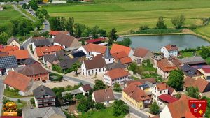 Sanierung der Kirche in Elsendorf beendet. Dorfplatz mit Weiher und Wirtshaus. Straße führt durch Elsendorf